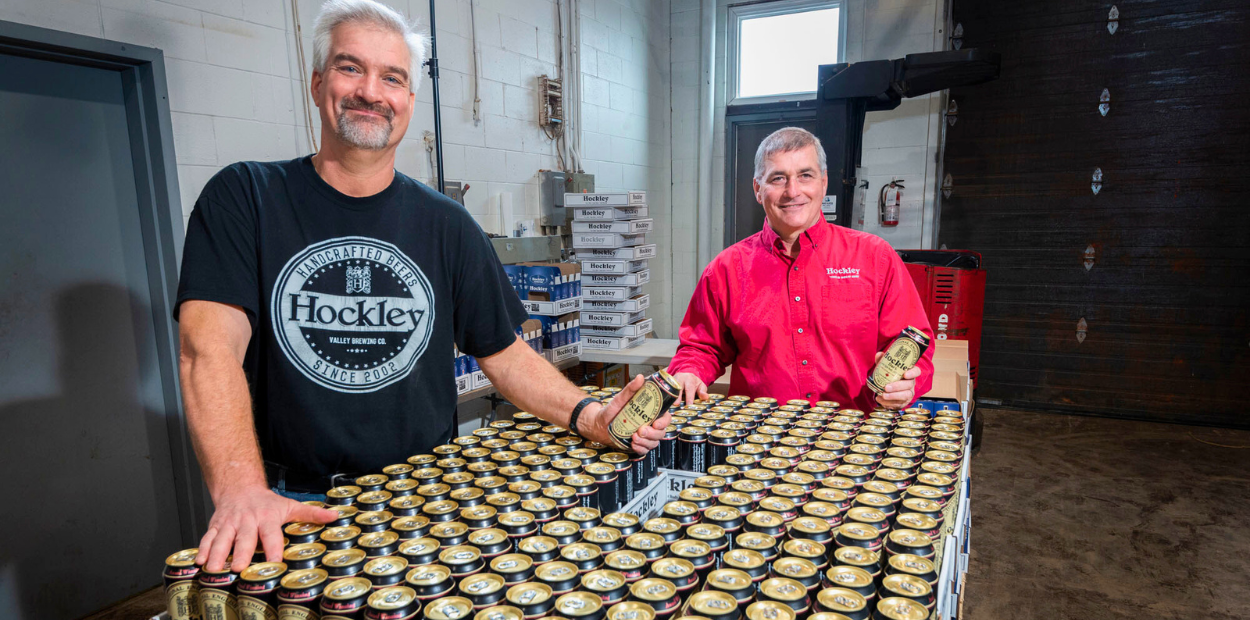 Two men standing in front of a pallet of beer cans.